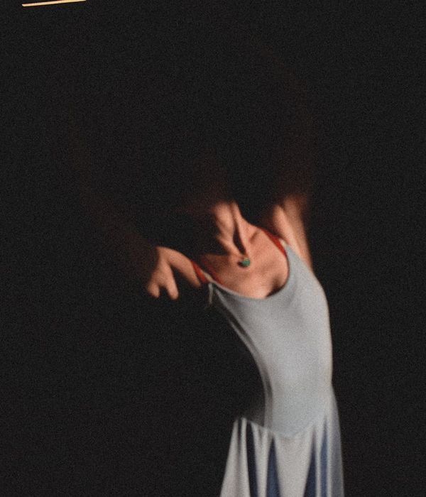 Woman performing a fluid, gentle aerobic movement in a dark studio with blue light accents.